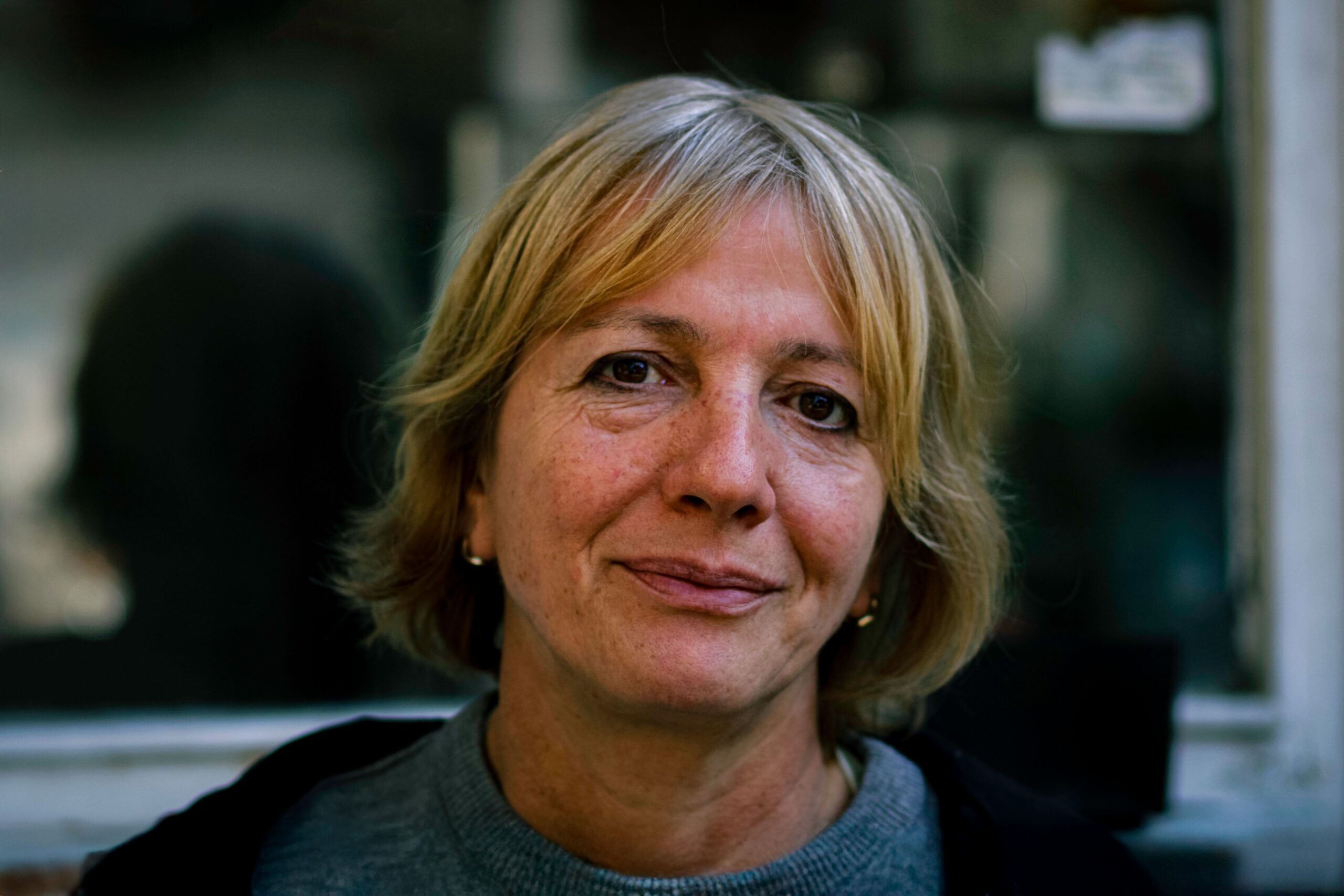 A candid portrait of a senior woman with short blonde hair, outdoors in natural light.